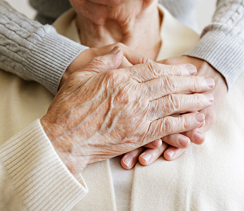 Am Foto sind Hände von zwei Personen zu sehen welche sich gegenseitig halten. Eine Hand ist von einer älteren Frau die zweite Hand ist von der Betreuerin.
