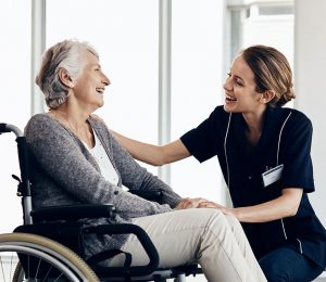 Am Foto ist eine ältere Dame im Rollstuhl mit einer Pflegekraft zu sehen.