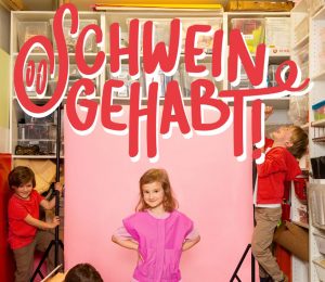 Am Foto sind vier Kinder, davon ein Mädchen und der Schriftzug Schwein gehabt zu sehen.