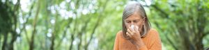 Am Bild sieht man eine Frau im Freien die sich wegen ihrer Allergiesymptome die Nase putzt.