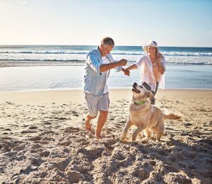 Am Bild ist ein älteres Ehepaar mit Hund am Strand zu sehen.